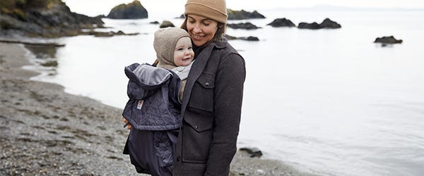 Women carrying baby with rain and wind cover nearby the sea